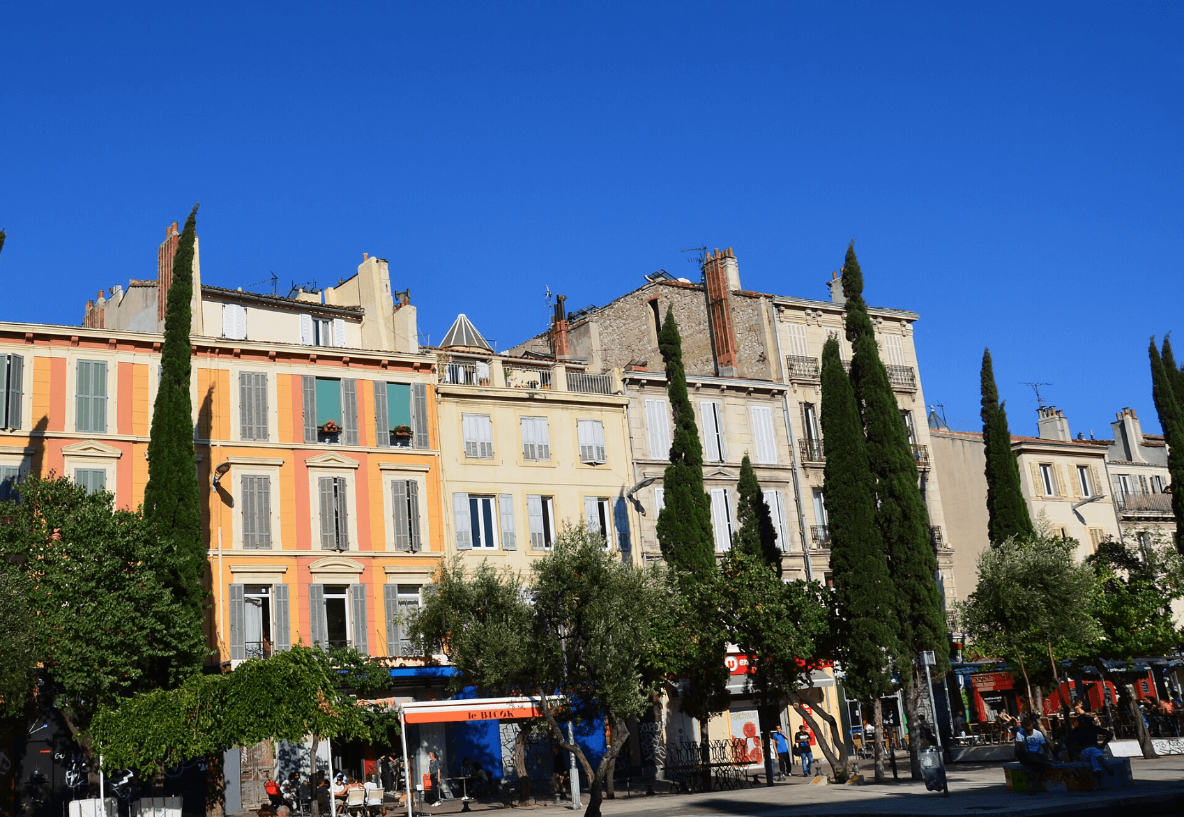 Bâtiments colorés et cyprès dans le quartier du Cours Saint-Julien à Marseille, un lieu animé connu pour son ambiance artistique et ses terrasses