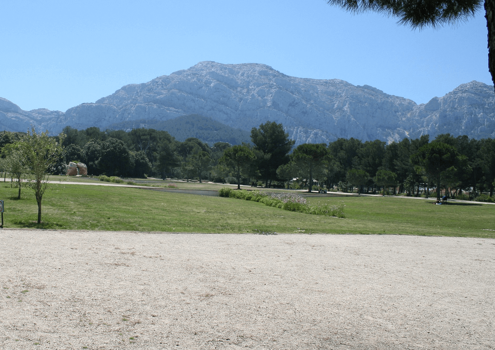 Vue dégagée du Parc Pastré à Marseille, avec de grandes étendues de pelouse, quelques arbres et, en arrière-plan, les majestueuses collines du massif de Marseilleveyre sous un ciel bleu clair.