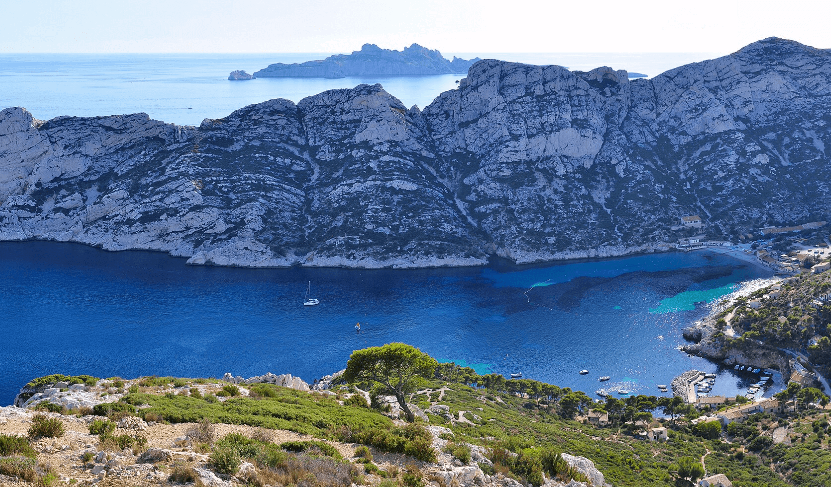Vue panoramique sur la calanque de Sormiou à Marseille, avec ses eaux turquoise, ses falaises calcaires escarpées, quelques bateaux à voile et un petit port niché au fond de la baie.Vue panoramique sur la calanque de Sormiou à Marseille, avec ses eaux turquoise, ses falaises calcaires escarpées, quelques bateaux à voile et un petit port niché au fond de la baie.