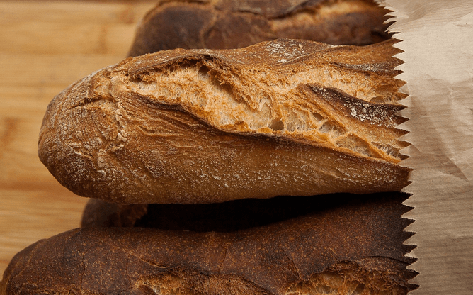 Baguettes de pain fraîches dans un sac en papier, posées sur une table en bois.