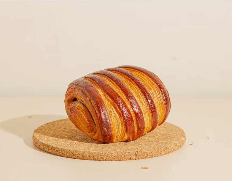 Pain au chocolat artisanal à la croûte dorée, posé sur un dessous de plat en liège.