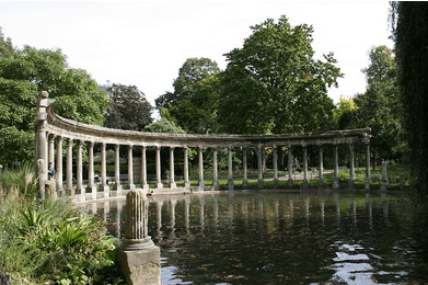 Parc Monceau à Paris avec lac, allées verdoyantes et colline surmontée d’un bâtiment pittoresque au coucher du soleil.